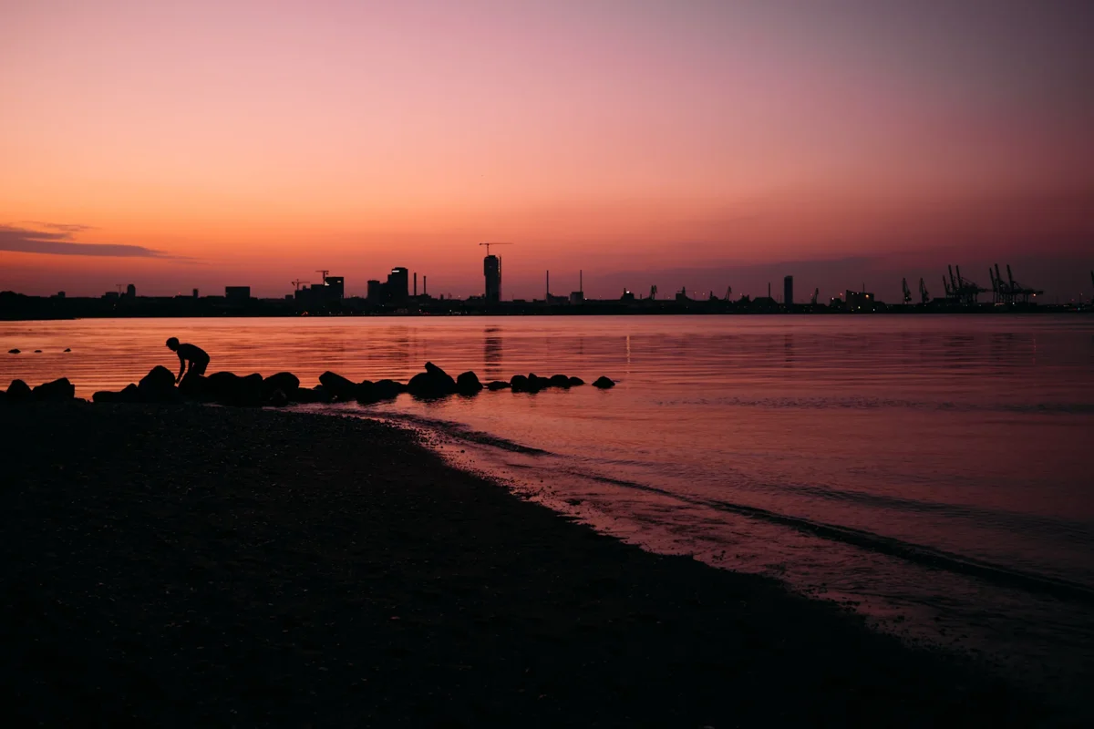Silhouette at the waterline at sunset with a city skyline and harbour cranes in the distance