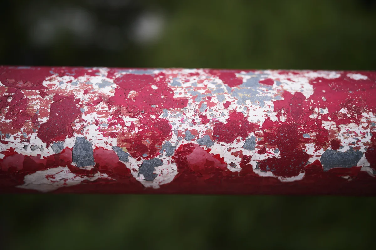 Close-up of peeling red paint on a metal railing against a green background