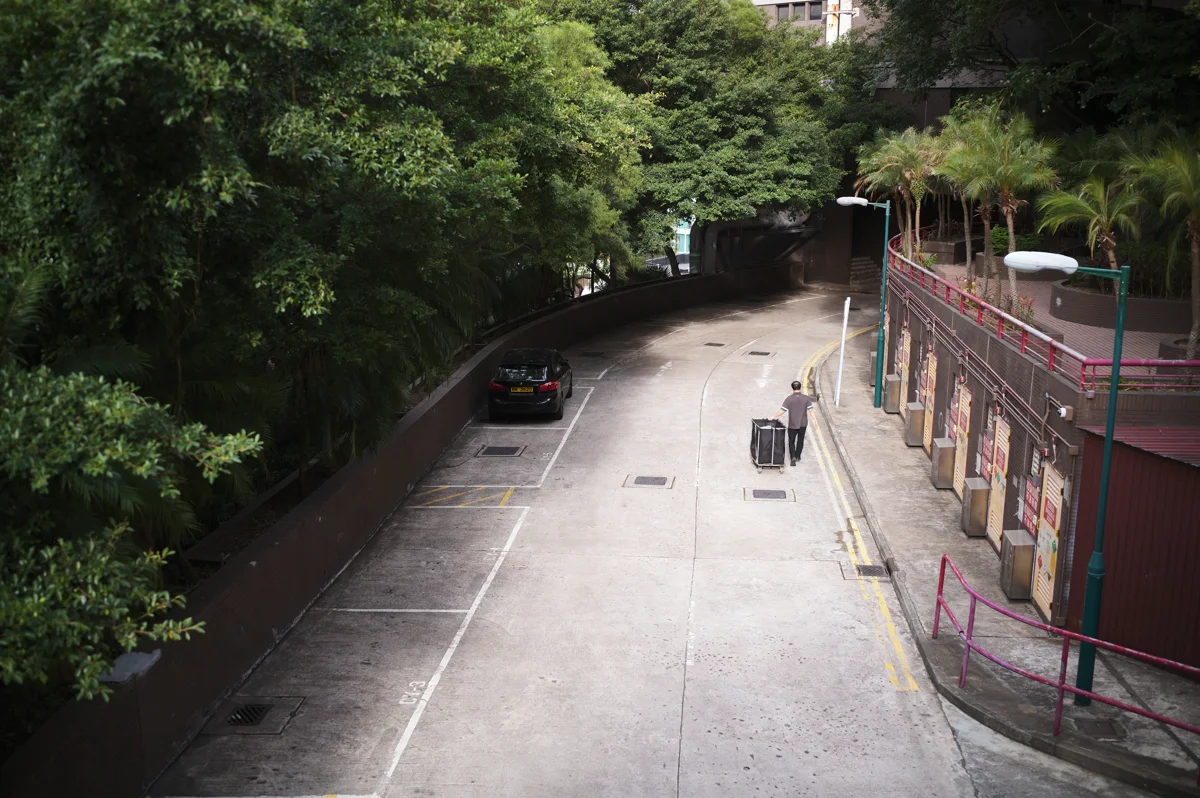 Elevated view of a curved city road with a person pushing a cart past parked cars