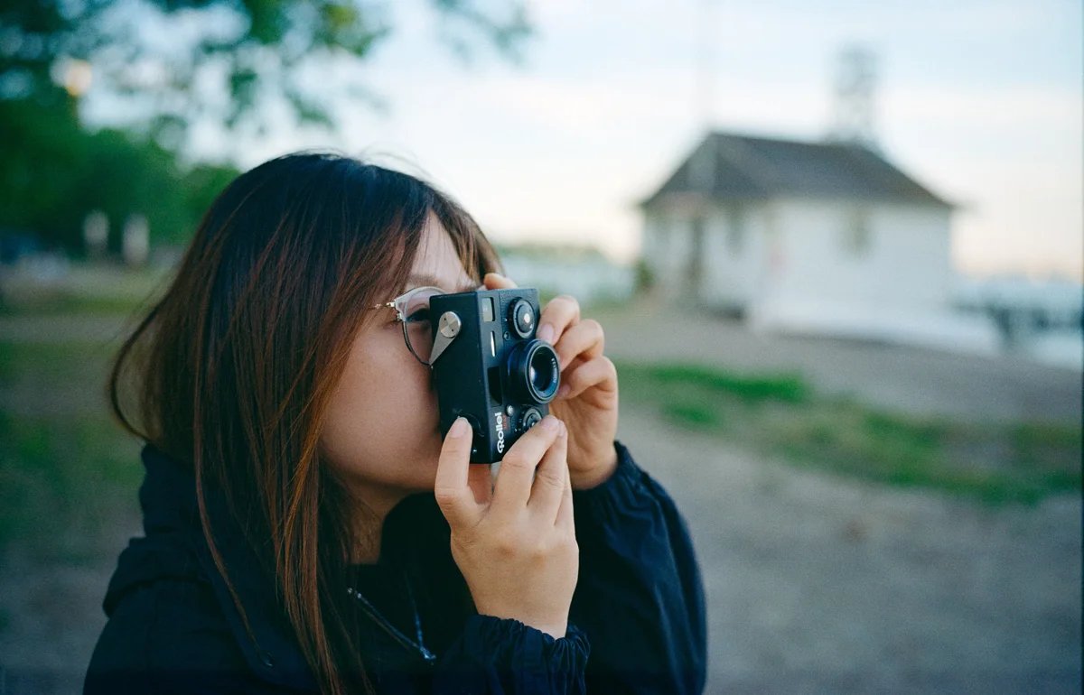 Woman photographing with a Rollei compact camera at dusk, shot on the Light Lens Lab 35mm f/2 Apochromatic